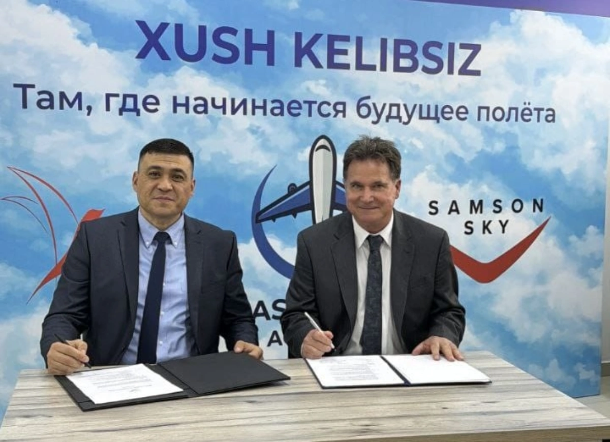 Two executives signing a partnership agreement in front of a banner featuring